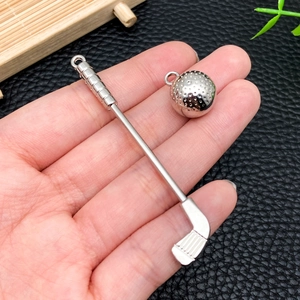 Detalle de pequeños dijes de palo y pelota de golf en la mano para mostrar el tamaño