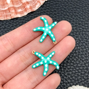 Close-up of small teal starfish charms with white polka dots for DIY jewelry making