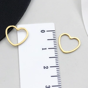 Dettaglio di ciondoli a cuore dorati con righello che mostra la misura di 1,5-1,8 cm