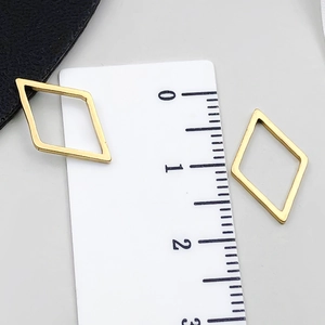 Dettaglio di ciondoli geometrici a rombo dorati su un righello per mostrare le misure