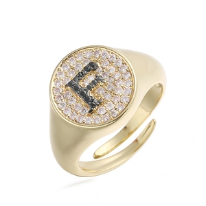 Detalle de anillo dorado con letra F, pavé de circonitas blancas y diamantes negros