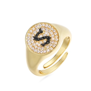 Detalle de anillo de sello dorado con letra S en piedras negras y pavé de circonitas