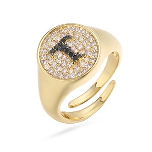 Detalle de anillo de sello dorado con micro-pavé de circonitas y letra T en negro