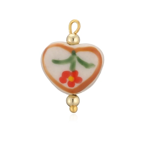 Détail macro d'un pendentif coeur en céramique avec motif floral peint à la main et perles d'or