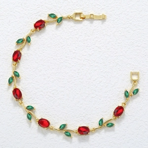 Detail of gold vine bracelet with red oval stones and green leaf gems on white background