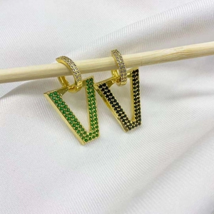 Close-up of V-shaped gold earrings with green and black micro-pave stones on white fabric