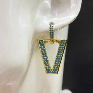 Detailed view of gold geometric V-shaped earrings with blue stones on a model's ear