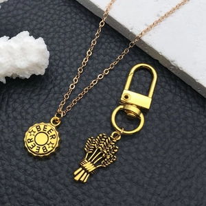 Vintage gold beer bottle cap necklace and barley keychain set on black leather background