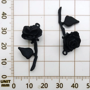 Macro shot of two matte black rose pendants with stems on a millimeter scale grid