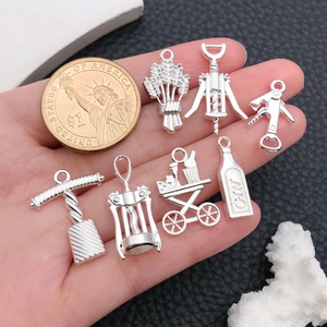 Macro detail of 7 silver alloy wine-themed charms next to a coin for size scale