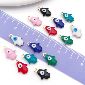 Colorful Hamsa Hand enamel charms with evil eye detail shown next to a ruler for scale