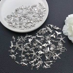Flat lay of antique silver sea creature charms on black leather and ceramic tray