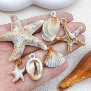 Beige acrylic starfish and seashell pendants held in hand for DIY jewelry making