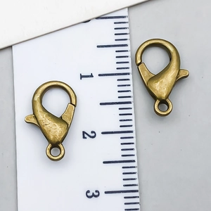 Pair of antique bronze alloy lobster clasps with jump rings shown on a size scale ruler