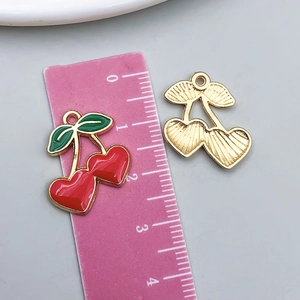 Detail view of heart-shaped cherry pendant charms with red enamel and gold finish