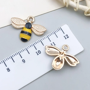 Yellow and black enamel bee charm accessory with textured wings and gold-tone alloy backing