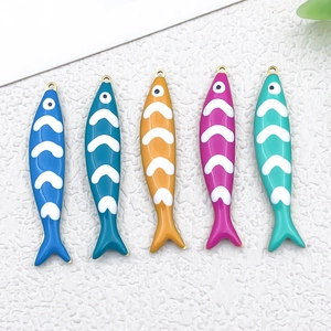 Flat lay of colorful fish enamel pendants in various shades with gold hooks on white surface