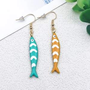Detail of colorful fish-shaped enamel earrings with gold hooks on a white background