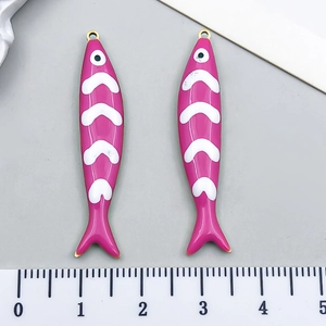 Detail view of pink and white enamel fish pendants with measurements on a gray scale ruler