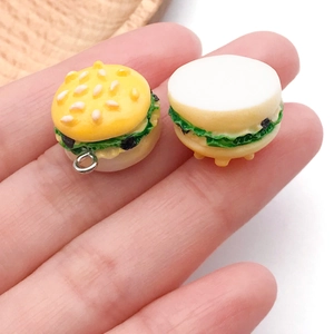 Close-up of mini realistic burger charms with lettuce and sesame seeds detail held in hand