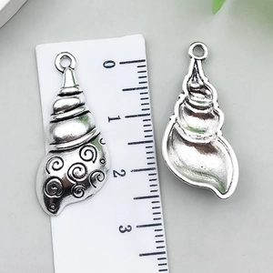 Detailed view of conch shell alloy pendant with swirl texture and ruler for scale