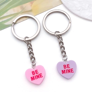 Close-up of pink and purple heart resin keychains with 'BE MINE' engraving on white background