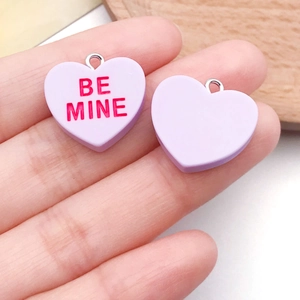 Detail of lavender resin heart charms with Be Mine text and silver rings for DIY jewelry