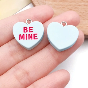 Handheld view of light blue resin heart pendants with Be Mine text and silver metal loops