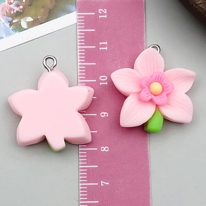 Macro detail of 3cm resin flower charms with pink petals, yellow stamens and metal rings