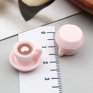Makroaufnahme von Miniatur-Kaffeetasse aus rosa Harz mit Herz-Latte-Art auf Untertasse