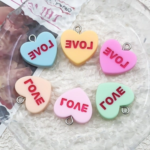 Macro detail of heart-shaped resin charms with LOVE print in various macaron colors