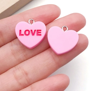 Detailed macro view showing both sides of a pink resin heart LOVE pendant with metal rings