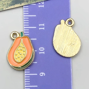 Detailed view of papaya-shaped enamel charms with size reference on a scale ruler
