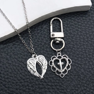 Close-up of silver angel wing pendant and hollow heart cross keychain on dark background