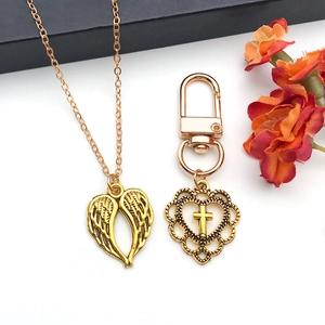 Close-up of antique gold heart angel wing necklace and hollow cross keychain accessory