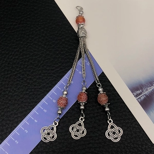 Ethnic alloy tassel pendant with orange beads and Celtic knot charms on a textured background