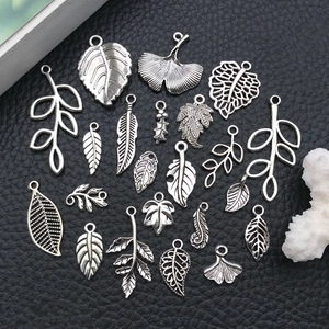 Macro shot of assorted silver alloy leaf pendants and charms on black leather background