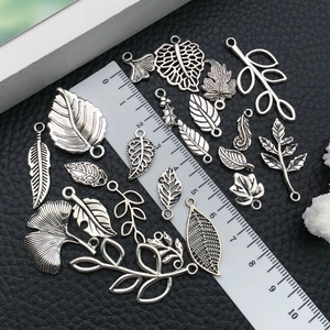 Macro shot of silver leaf pendants and feather charms with size scale on black leather