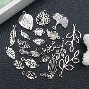 Assorted vintage silver alloy leaf charms for DIY jewelry making on black leather background