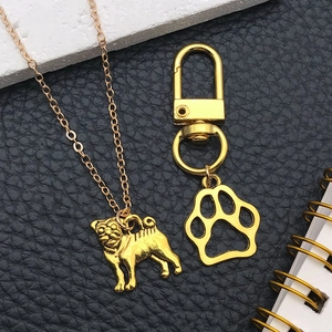 Detail of gold pug necklace and hollow paw print keychain on black leather background