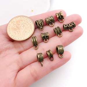 Détail de dix bélières en alliage de bronze antique pour bijoux DIY à côté d'une pièce