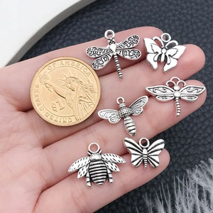 Antique silver insect charms for DIY jewelry held in hand with coin for scale