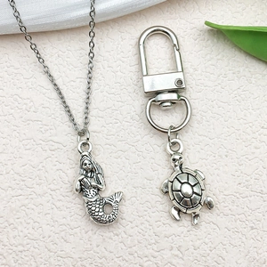 Detailed silver mermaid necklace and turtle keychain with vintage texture and green leaf accents