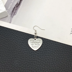 Detail eines silbernen Herzohrrings mit der Gravur You are always in my heart