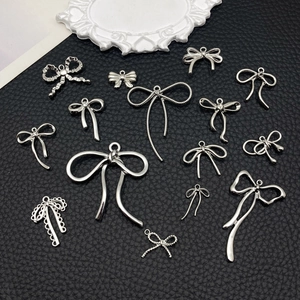 Detalle de colgantes de lazo plateados y accesorios para joyería sobre fondo de cuero negro