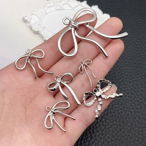 Juego de seis colgantes de lazo plateados para joyas DIY mostrados sobre una mano humana