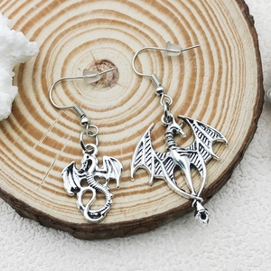 Vintage silver dragon drop earrings featuring asymmetrical mythical wing designs on wood