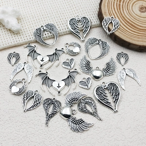 Macro shot of silver punk wing and heart pendants on a textured cream surface