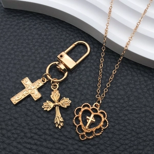 Detail view of gold cross keychain and heart necklace charms with a vintage finish