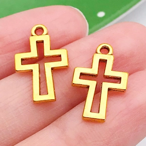 Close-up of a gold hollow cross pendant held on a finger to show its actual size